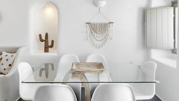 Uma sala de jantar moderna com mesa de vidro, cadeiras brancas, uma decoração de cacto e um candelabro.