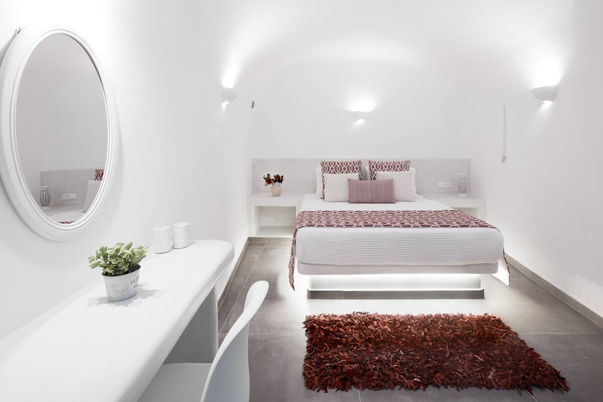 A modern bedroom with a large bed, bedside tables, a mirror, and a small plant.