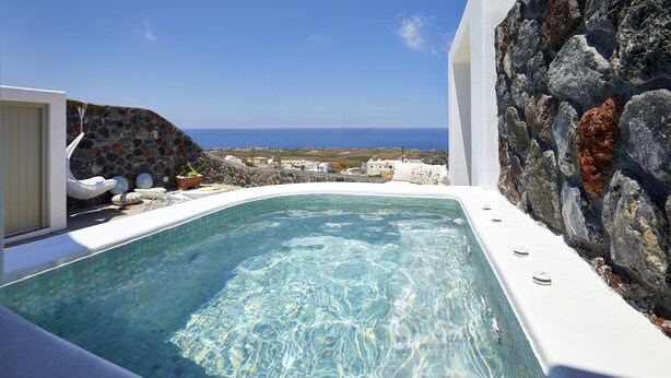 A clear blue pool with a stone wall and a view of the sea. - Mellow Luxury Cave (Santorini)