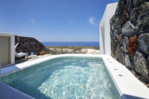 Een helderblauw zwembad met een stenen muur en uitzicht op zee.