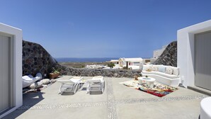 A modern outdoor living area with a stone wall, white furniture, and a view of the sea. - Mellow Luxury Cave (Santorini)