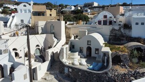 A white building with a stone wall and a sign that reads "MELTOW LUXURY CAVE". - Mellow Luxury Cave (Santorini)