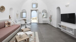 A modern living room with a sofa, chairs, a TV, and a view to the outside. - Mellow Luxury Cave (Santorini)