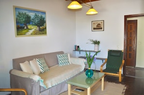 A living room with a sofa, a glass coffee table, a chair, a painting, and a door.