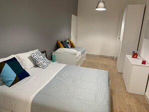 A bedroom with a large bed, a smaller bed, a nightstand, a wardrobe, and a hanging light fixture.