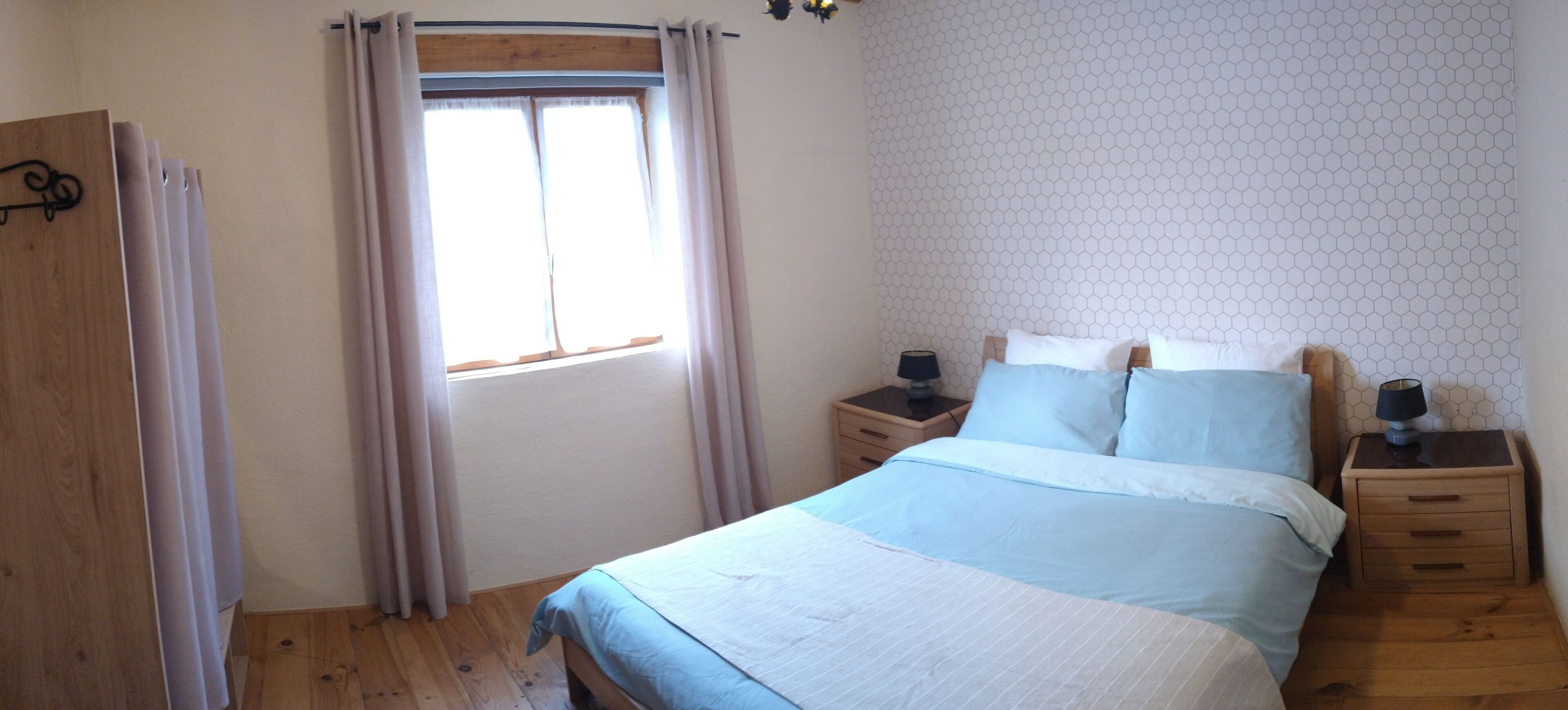 Ein Schlafzimmer mit einem Bett, zwei Nachttischen, einem Fenster mit Vorhängen und einer Wand mit sechseckigem Muster.