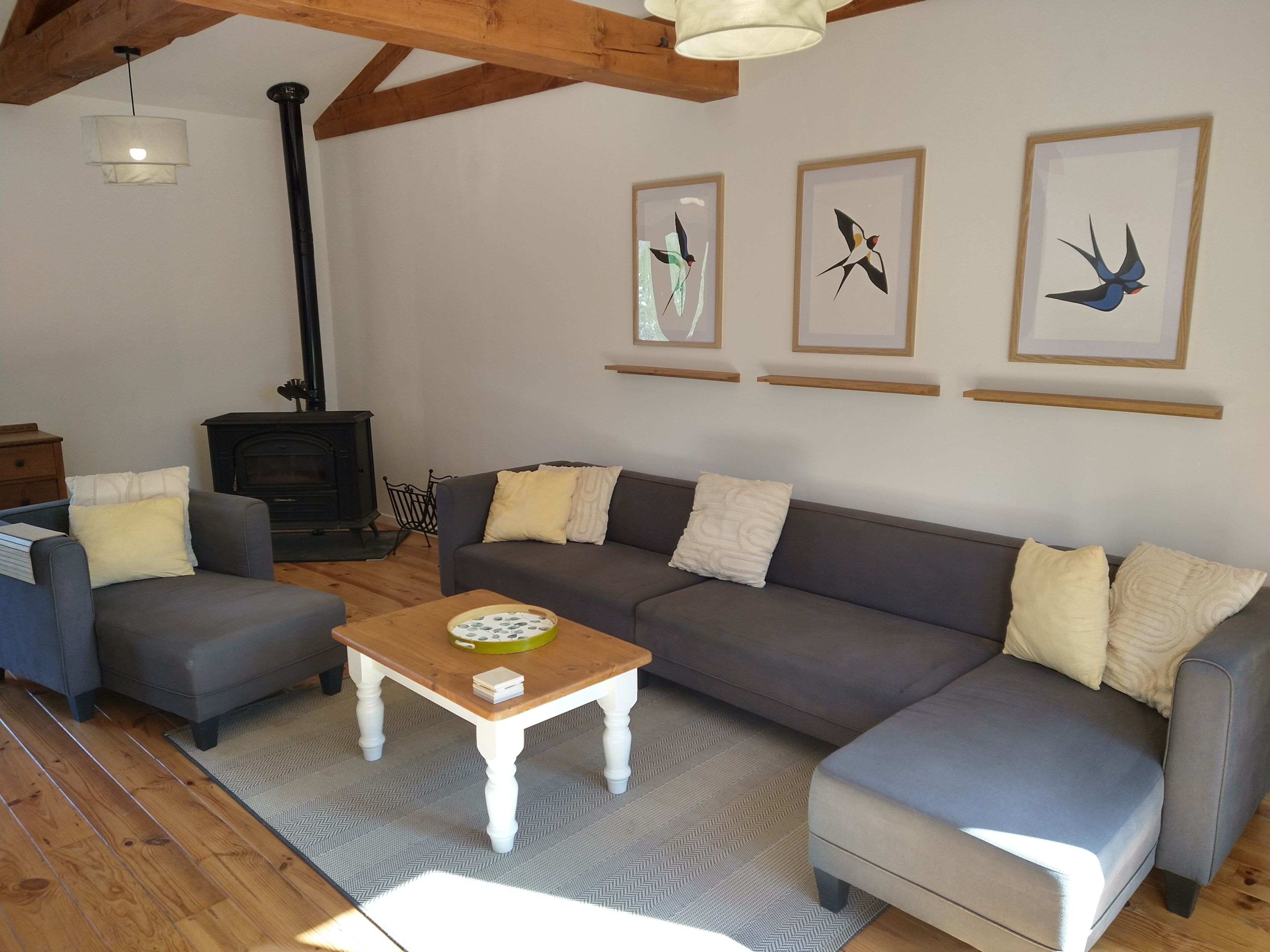 A living room with a sofa, two armchairs, a coffee table, a fireplace, and three framed bird paintings on the wall.