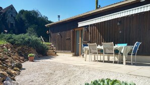 Un patio con mobiliario exterior, un muro de piedra y un edificio de madera con una puerta.