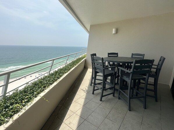 A balcony with a view of the ocean, a table with chairs, and a small wall-mounted light fixture.