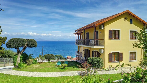 A two-story yellow building with a red roof, a balcony, and a view of the sea. - Eleni's Apartments & Studios (Corfu)