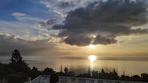 A coastal view with a sunset over the water, a balcony with outdoor seating, and a distant mountain range. - Eleni's Apartments & Studios (Corfu)