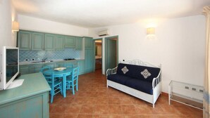 Una cocina compacta con armarios color turquesa, una mesa de comedor con sillas y un sofá blanco con cojines decorativos.
