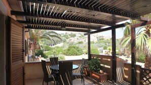 Un espacio al aire libre con techo, una mesa, sillas, una planta en maceta y vistas a un paisaje natural.