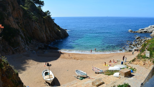 Une plage avec des bateaux, une falaise rocheuse et la mer.