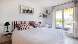 Une chambre avec un grand lit, des oreillers à rayures, une table de chevet avec une lampe, un tableau au mur et une vue sur l’extérieur par une porte coulissante.