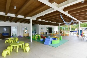 Children can play and explore in this spacious indoor play area with a high ceiling, colorful play structures, and tables with toys and books.