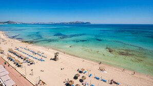 Ein Strand mit klarem türkisblauem Wasser, Liegestühlen und Sonnenschirmen.