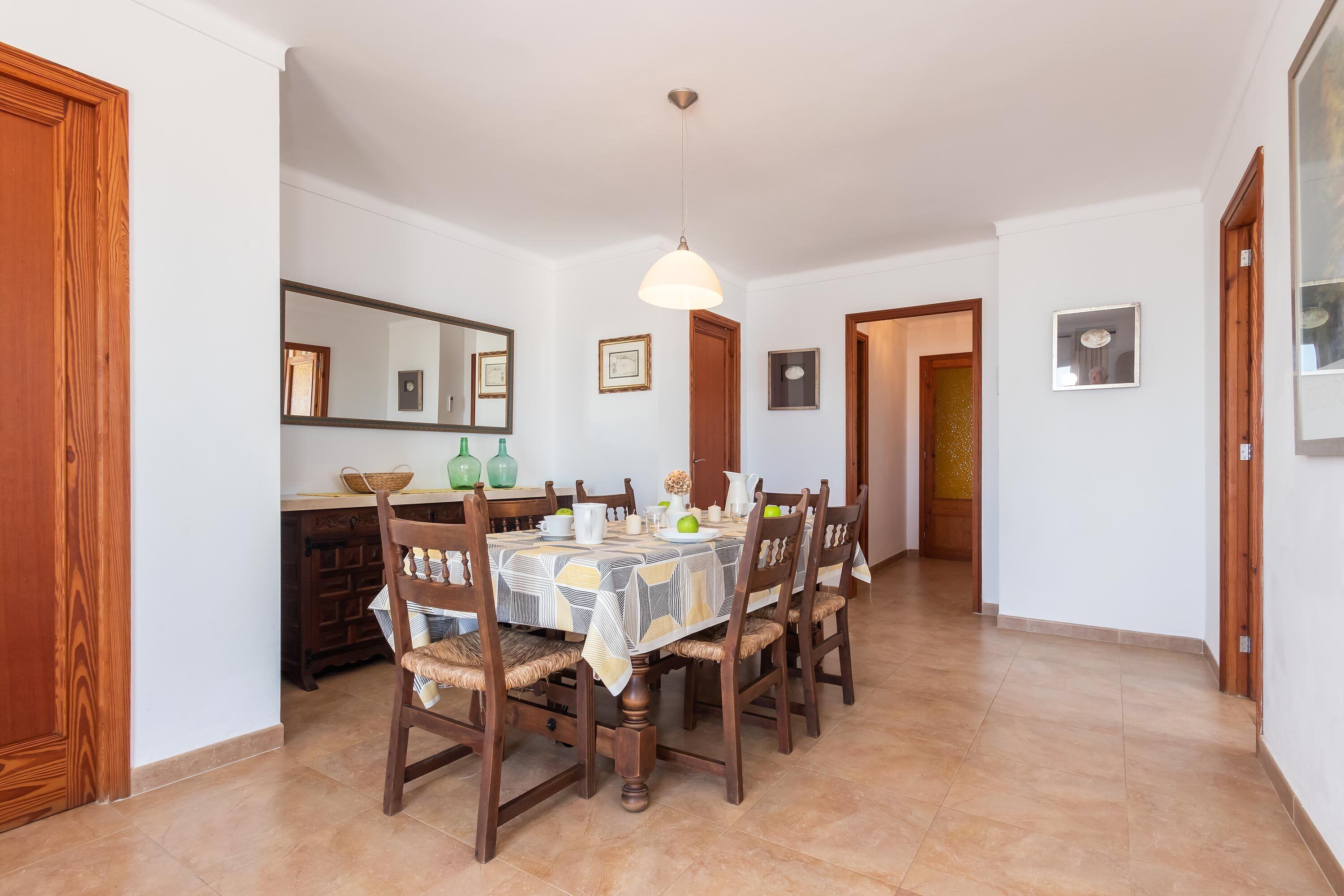 Un comedor con una mesa dispuesta para cuatro personas, rodeada de sillas de madera, un candelabro y un espejo en la pared.