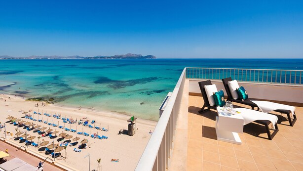 Blick auf den Strand vom Balkon aus, mit Liegestühlen und Sonnenschirmen.