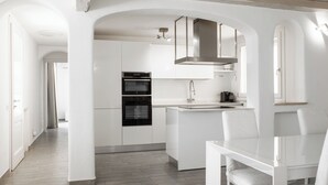 A modern kitchen with white cabinetry, a built-in oven, and a dining area with a white table and chairs.