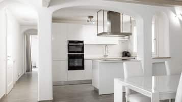 A modern kitchen with white cabinetry, a built-in oven, and a dining area with a white table and chairs.