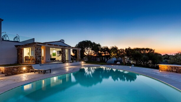 A poolside area with a stone building, lounge chairs, and a clear sky.