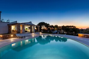 Zona junto a la piscina con un edificio de piedra, sillas de descanso y cielo despejado.