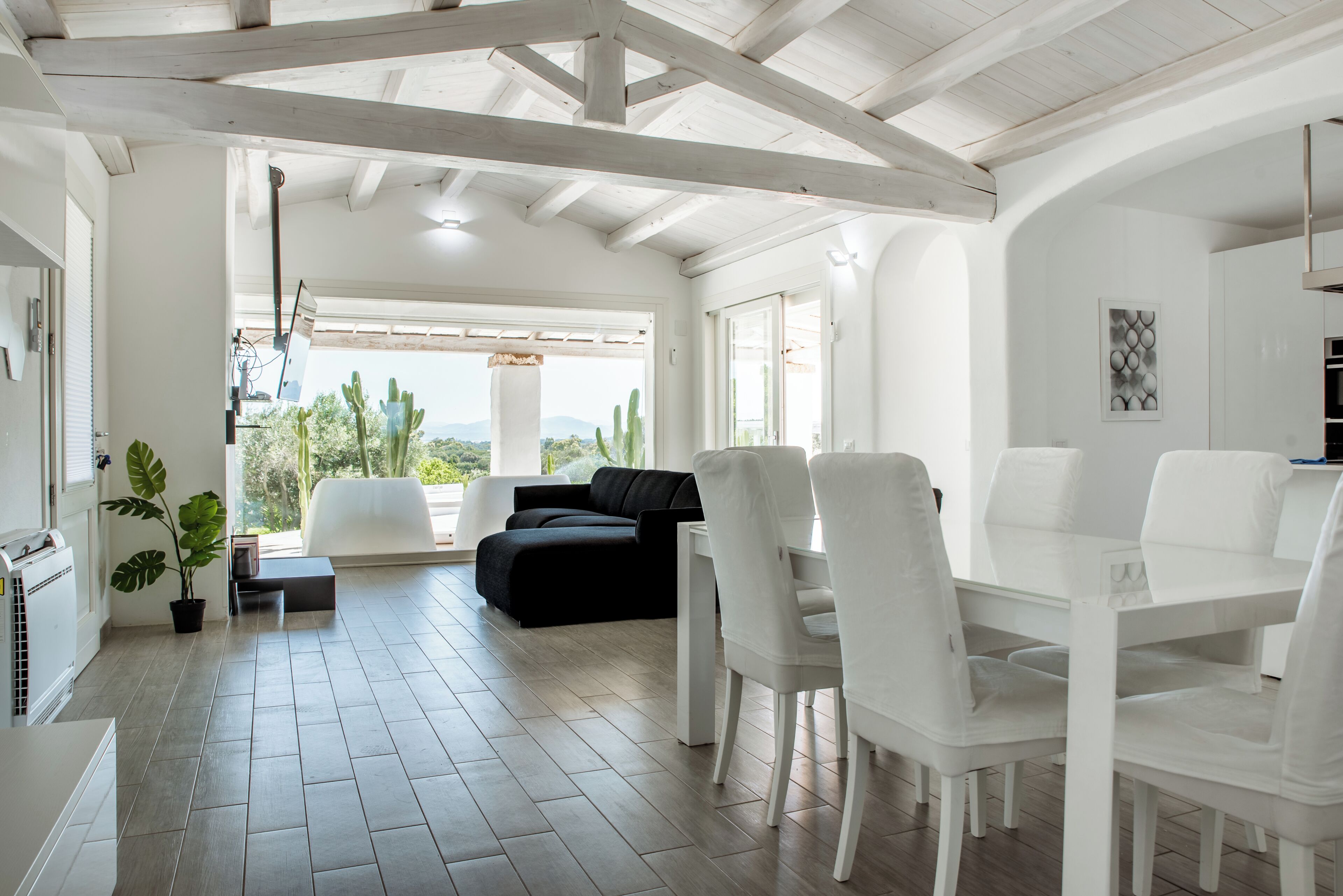 A spacious living area with a black sofa, white chairs, and a dining table.