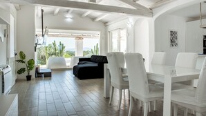 A spacious living area with a black sofa, white chairs, and a dining table.