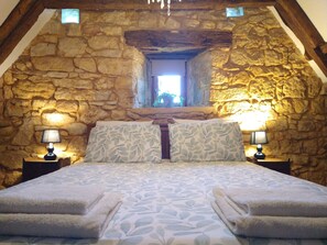 A bedroom with a stone wall, a sloped ceiling, a bed with leaf-patterned pillows, and two bedside lamps. - Les Papillons 4/6, Pool, Balcony, Garden & Courtyard, Top Location & Activities (Domme)