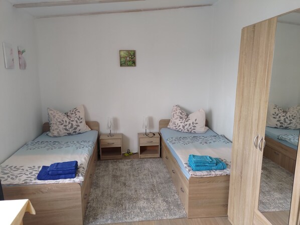 Een slaapkamer met twee eenpersoonsbedden, nachtkastjes, een spiegel en een klein vloerkleed.