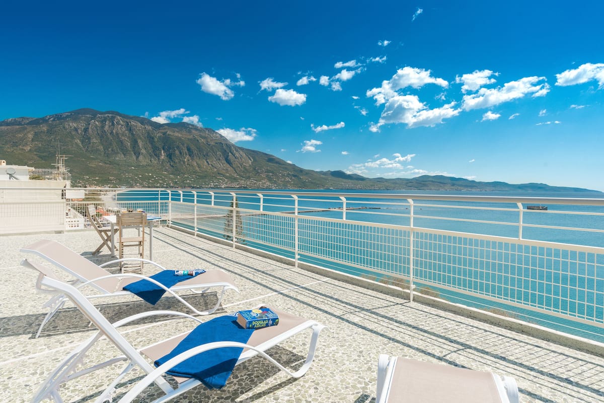 Zona junto a la piscina con sillones de descanso y vistas al mar y a las montañas.