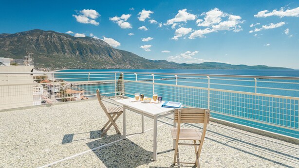 Una terraza con una mesa, sillas y vistas al mar y a las montañas.