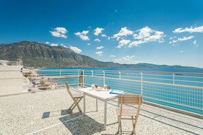 A terrace with a table, chairs, and a view of the sea and mountains. - Seafront Penthouse LEO (Kalamata)