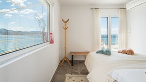 Un dormitorio con un ventanal grande, una lámpara de pie de madera, un banco y una cama con toallas enrolladas.