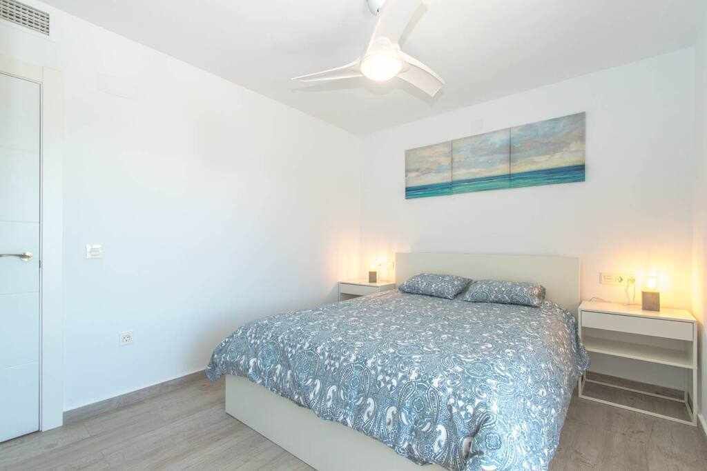 Une chambre à coucher avec un lit, un ventilateur de plafond, une table de chevet, un tableau et une porte.