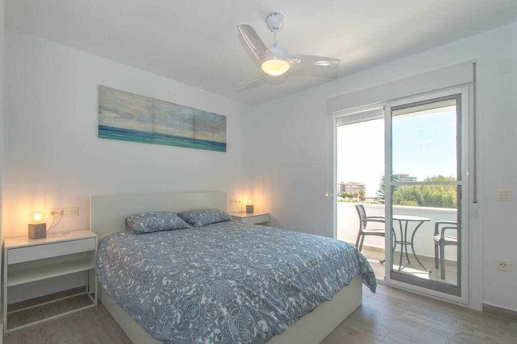 A bedroom with a bed, bedside tables, a ceiling fan, a painting, and a sliding glass door leading to an outdoor area.