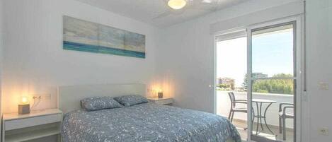 A bedroom with a bed, bedside tables, a ceiling fan, a painting, and a sliding glass door leading to an outdoor area.