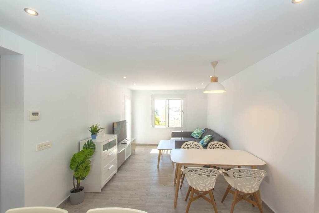 Une cuisine moderne avec des meubles blancs, un coin repas avec une table et des chaises blanches, et un salon avec un canapé et un téléviseur.