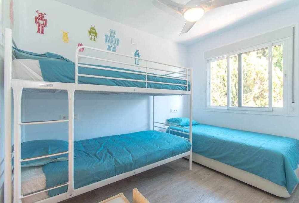 A bunk bed room with a window, white walls, and a ceiling fan.