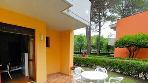 Un patio con suelo de madera, sillas de plástico blanco y una mesa.