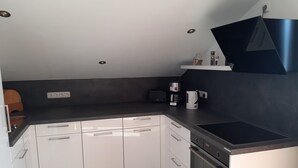 Eine kleine Küche mit weißen Schränken, einer schwarzen Arbeitsplatte, einem eingebauten Ofen und einer Kaffeemaschine.