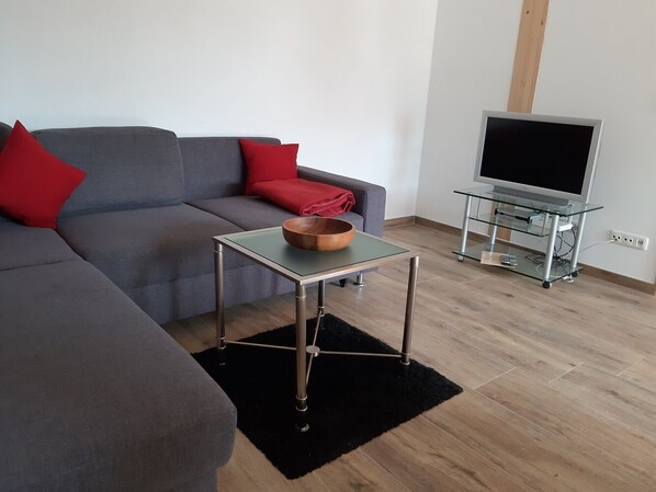 A modern living room with a grey sofa, red cushions, a glass-top coffee table, and a flat-screen TV on a stand. - Bright, comfortable, and tastefully furnished apartment with a south-facing balcony (Hausham)