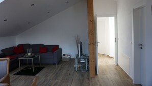 Ein modernes Wohnzimmer mit einem grauen Sofa, roten Kissen, einem Glastisch und einer Holzbalkenkonstruktion.