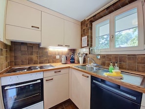 Una cocina con estufa, horno, pileta y lavavajillas. Hay una ventana sobre la pileta.