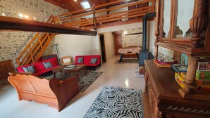 A rustic interior with a wooden staircase, a red sofa with patterned cushions, a wooden table, and a zebra-patterned rug. - Large stone house with enclosed garden, pets allowed (Marcillat-en-Combraille)