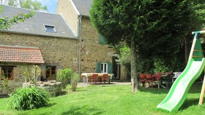 A stone building with a tiled roof, a grassy yard, a table with chairs, and a green slide. - Large stone house with enclosed garden, pets allowed (Marcillat-en-Combraille)