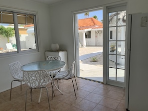 A small, private dining area with a round table and white chairs, a small cabinet, and a window overlooking a courtyard with a tiled floor and a palm tree.