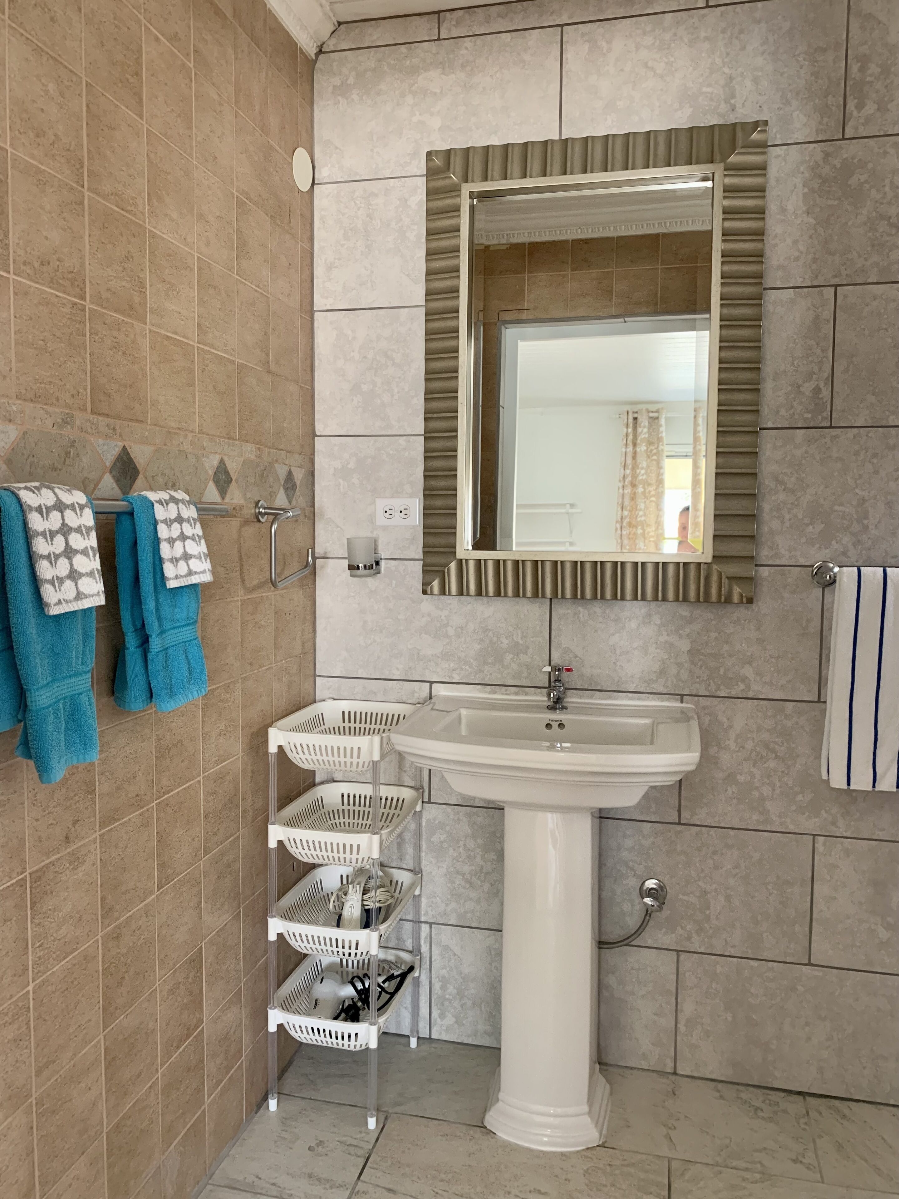 A bathroom with a white sink, a mirror with a decorative frame, and a towel rack with patterned and solid blue towels.