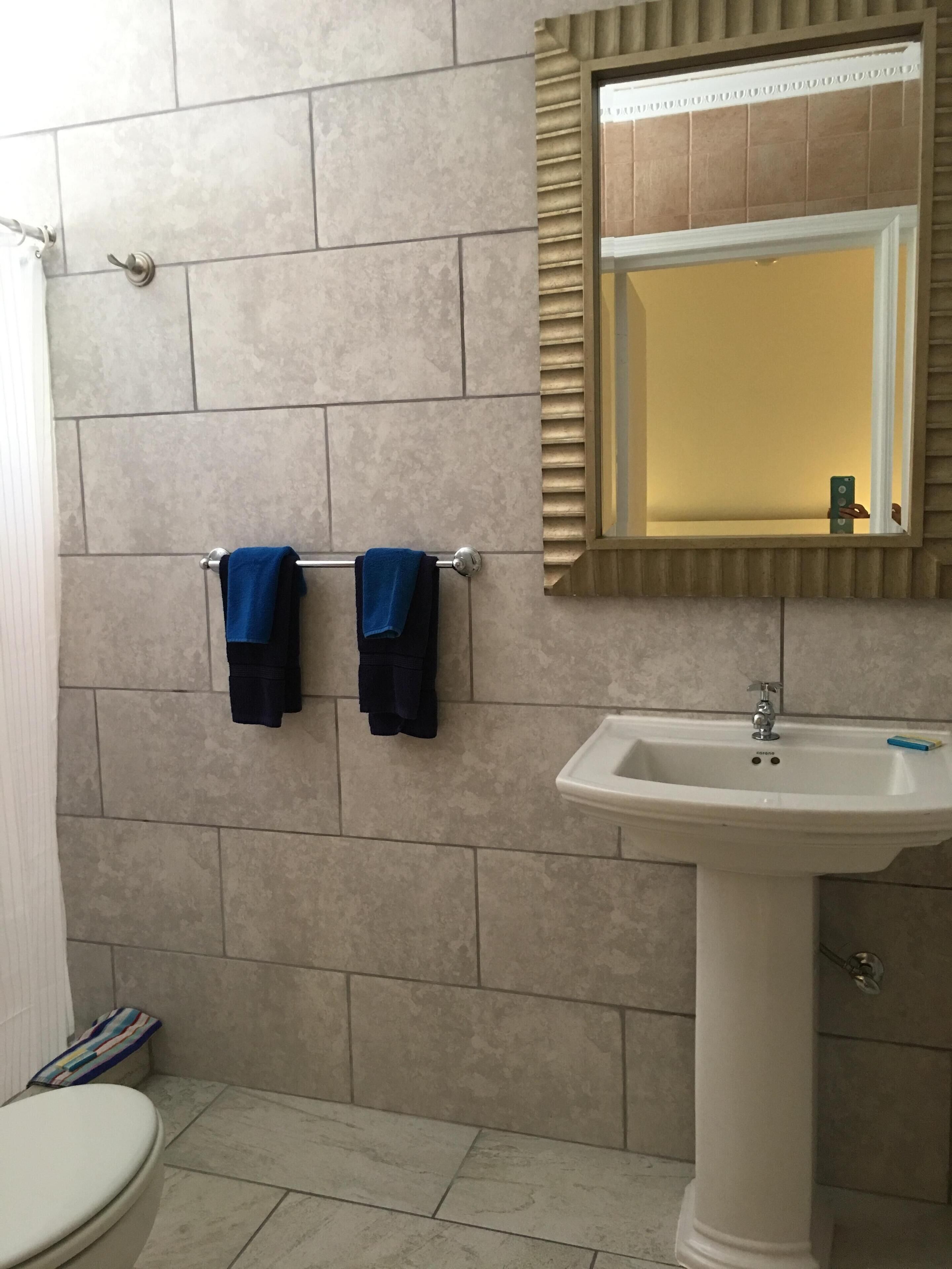 Une salle de bain avec un lavabo blanc, un miroir et deux serviettes suspendues à un porte-serviettes.